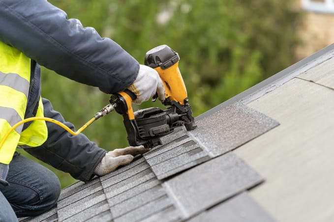 Workman using pneumatic nail gun installing shingles on a roof